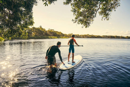 Ein Mann und ein Kind stehen gemeinsam auf einem Stand-up-Paddleboard.
